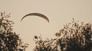 Tandem Paramotor Süzülüyor. İki adam ağaçların üzerinde havada süzülüp uçuyor. Siluetler