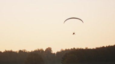 Tandem Paramotor Süzülüyor. İki adam ağaçların üzerinde havada süzülüp uçuyor. Siluetler