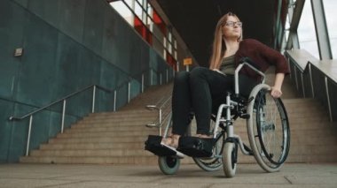 Genç, cesareti kırılmış, tekerlekli sandalyeli, merdivenin önünde oturan beyaz kadın çevreye erişilebilir bir yol arıyor.