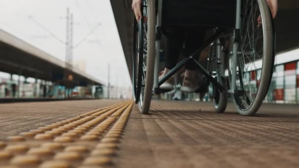 Angle bas, jeune femme tournant les roues du fauteuil roulant sur la gare — Video