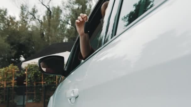 Nytt bilköp. Ung lycklig kvinna vinka med bilnycklarna genom änkan av fordonet — Stockvideo