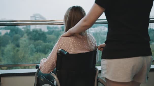 Carriera, donna che accarezza la spalla della giovane donna sulla sedia a rotelle sul balcone — Video Stock