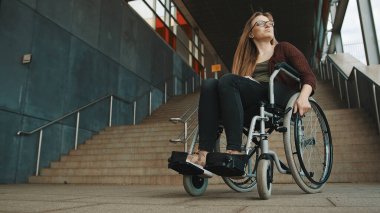 Genç, cesareti kırılmış, tekerlekli sandalyeli, merdivenin önünde oturan beyaz kadın çevreye erişilebilir bir yol arıyor.