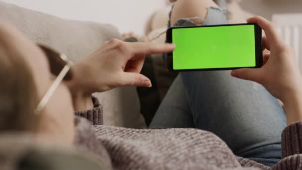 스마트폰 녹색 화면을 들고 소파에 앉아 손을 흔들고 있는 젊은 여성. 비디오 통화 — 비디오