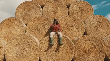 Afrikalı siyah çiftçi samanlıkta oturuyor ve telefonla konuşuyor.