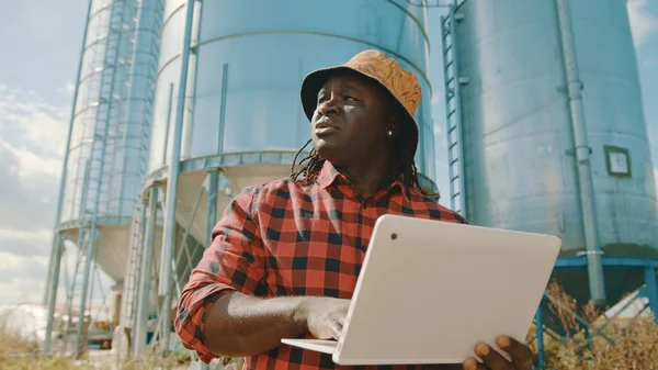 African farmer using laptop in front of the silo storage system
