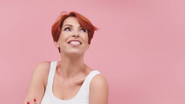 Orta yaşlı, güzel, kızıl saçlı bir kadın pembe arka planda izole edilmiş, mutlu ve havalı bir gülümseme takınıyor. Şanslı kişi..