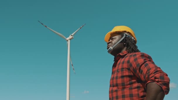 Ung ingenjör afrikan man med gul hjälm arbetar i vindkraftverk gård — Stockvideo