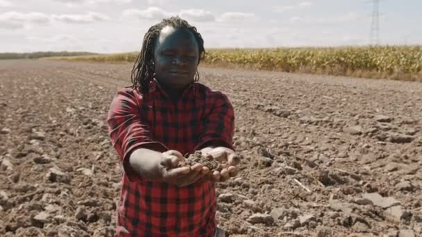 Un fermier africain tenant de la terre dans ses mains. Plan moyen à la ferme — Video