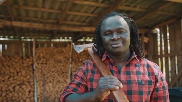 Afrikaanse houthakker in de winkel met gestapelde logs voor de winter knikken zijn hoofd met een glimlach — Stockvideo