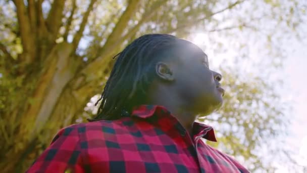 L'homme africain prend un grand souffle lève les mains et lève les yeux vers le ciel. Rayons solaires traversant l'arbre. Concept d'espoir et de prière — Video