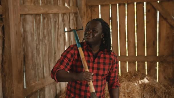 Agricultor africano sosteniendo tenedor sobre su hombro en el granero — Vídeo de stock