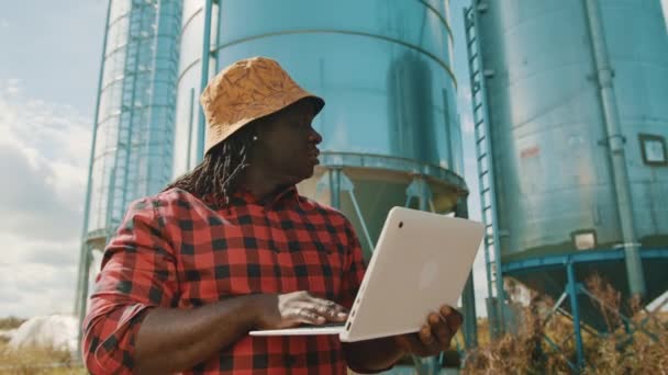 Agricoltore africano che utilizza il computer portatile di fronte al sistema di stoccaggio silo — Video Stock