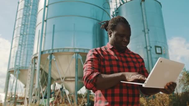 Αφρικανός αγρότης που χρησιμοποιεί φορητό υπολογιστή μπροστά από το σύστημα αποθήκευσης σιλό — Αρχείο Βίντεο
