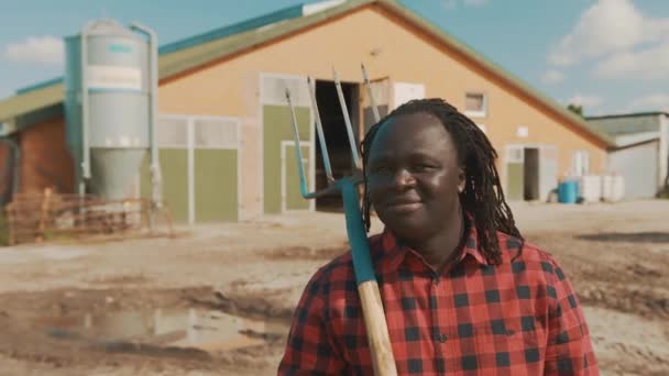 Jovem fazendeiro africano segurando garfo sobre a alma e acenando com a cabeça na frente do sistema de silo — Vídeo de Stock