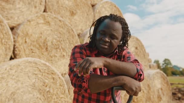 Jeune agriculteur africain nettoyant la sueur avec la main de son front. Foin rouleau pile en arrière-plan — Video