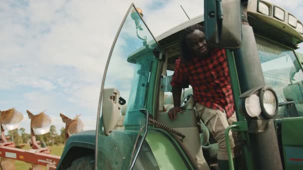A fiatal afrikai farmer kiszáll a zöld traktorból a farmon. — Stock videók
