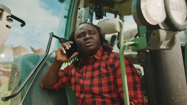 Afrikai farmer beszél az okostelefonon, miközben támaszkodik a zöld traktor — Stock videók