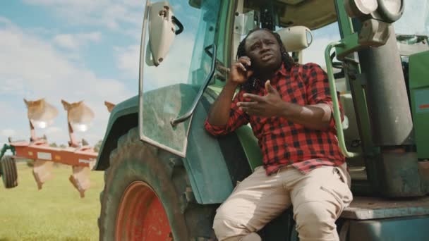 Agricoltore africano che parla sullo smartphone mentre si appoggia sul trattore verde — Video Stock