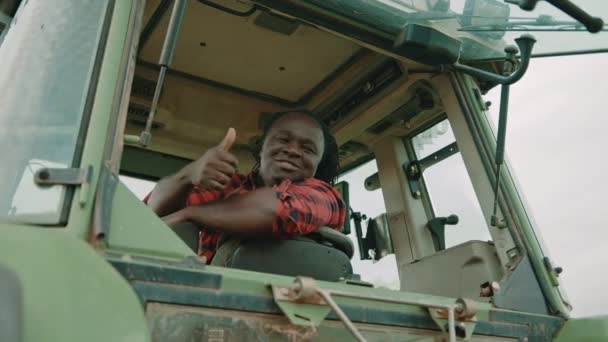 Jovem agricultor africano sentado na cabine do trator e mostrando os polegares para cima como aprovação — Vídeo de Stock