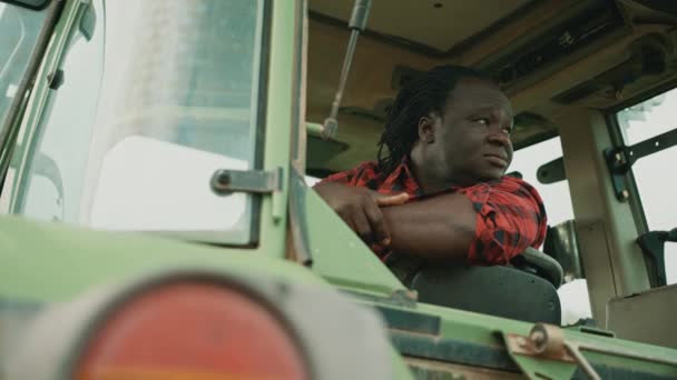 Cansado joven agricultor africano sentado en la cabaña del tractor y mirando a su alrededor — Vídeos de Stock