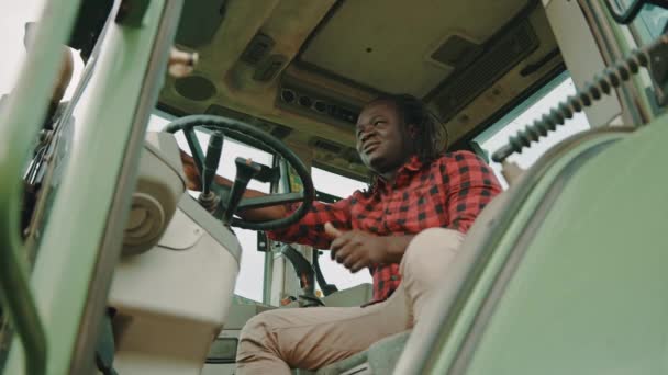 Νεαρός Αφρικανός αγρότης που κάθεται στο βαγόνι των τρακτέρ και δείχνει τους αντίχειρές του ως έγκριση. Χαμηλή γωνία βολής — Αρχείο Βίντεο