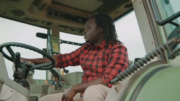 Genç Afrikalı çiftçi traktör kabininde oturuyor ve arka pencereden bakıyor. — Stok video