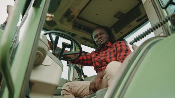 Jovem agricultor africano sentado na cabine do trator e acenando com a cabeça — Vídeo de Stock