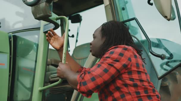 Young african man, farmer getting into tractor cabin — Stock Video