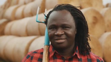Omzunda tırmıkla başını samanlığın önüne sallayan Afrikalı genç çiftçinin portresi.