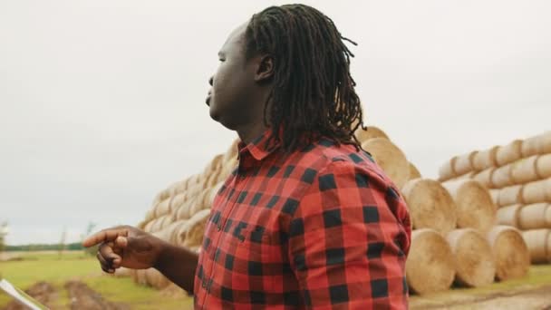 Fiatal afrikai férfi, táblagépen dolgozik a szénakazal előtt. Intelligens gazdálkodás — Stock videók