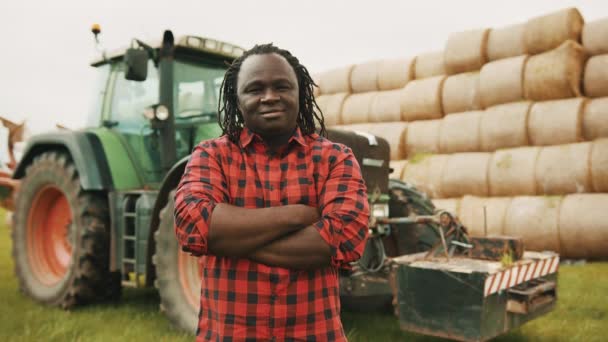 Fiatal afrikai férfi bólogatott, mint jóváhagyás keresztbe tett kézzel a mellkasán előtt traktor és szénakazal. Hüvelykujj fel! — Stock videók