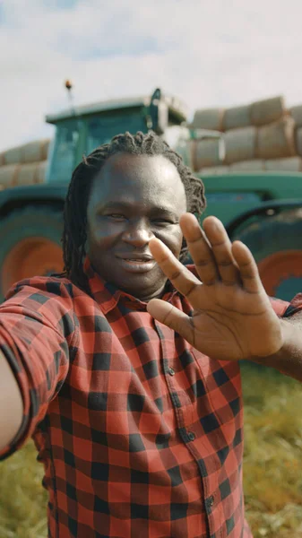 Videohovor. Africký farmář mává na smartphone camere před traktorem — Stock fotografie