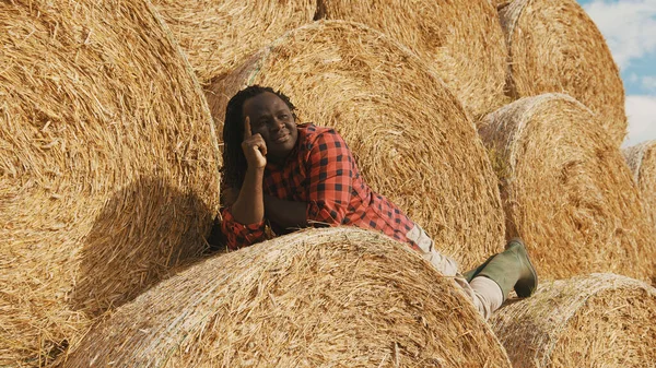 Young happy african farmer lying on the stack of hay rolls and resting — Stock Photo, Image