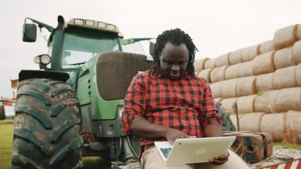 Upp med tummen. Ung afrikansk bonde som använder surfplatta sittande på grön traktor. Haystack i bakgrunden — Stockvideo