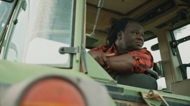 Yorgun genç Afrikalı çiftçi traktör kabininde oturuyor ve etrafa bakıyor.