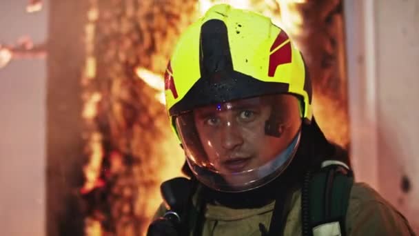 Potrait of young firefighter in full uniform in front of burning house — Stock Video