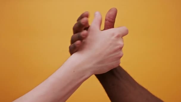 Mains noires et blanches se tenant ensemble, haut cinq secouent isolé sur le fond orange. Gros plan — Video
