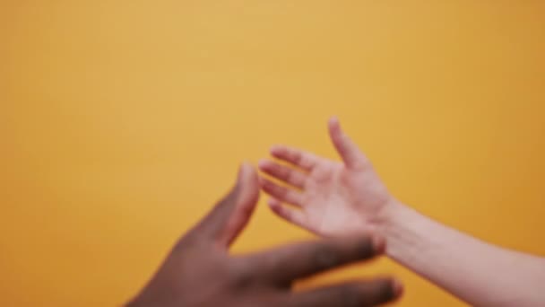 Fekete-fehér kéz tartja össze, pacsizás elszigetelve a narancssárga háttéren. Közelről. — Stock videók