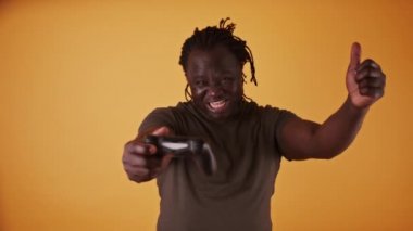 Oyun kumandalı heyecanlı Afrikalı adam turuncu arka planda izole edildi. Oyunu kazanırken mutluydu.