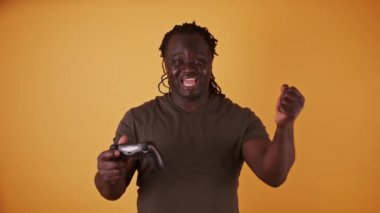 Oyun kumandalı heyecanlı Afrikalı adam turuncu arka planda izole edildi. Oyunu kazanırken mutluydu.