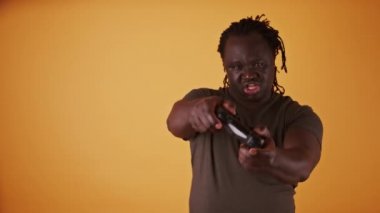 Turuncu arka planda oyun kontrolörü olan Afrikalı bir adam izole edilmiş.