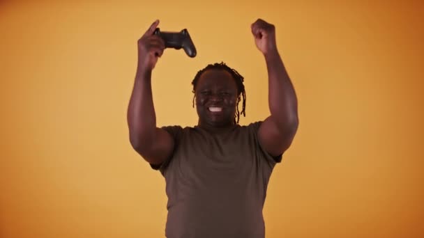 Opgewonden Afrikaanse man met game controler geïsoleerd op oranje achtergrond blij als hij won het spel — Stockvideo