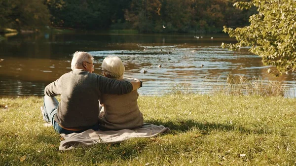 Älteres grauhaariges Paar sitzt an einem Herbsttag auf der Bank am Fluss — Stockfoto