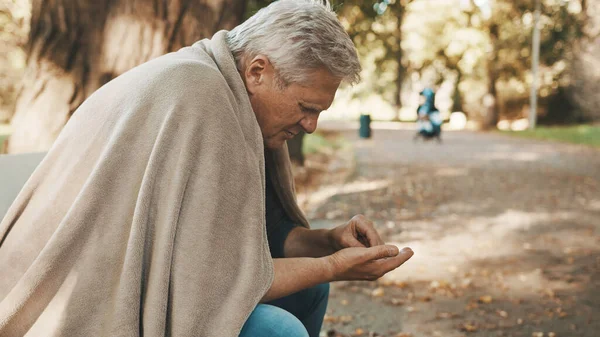 Poor older homeless man counting left coins in the park on autumn day