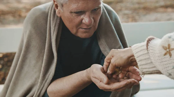 Бедный пожилой бездомный мужчина получает монеты от женщины — стоковое фото