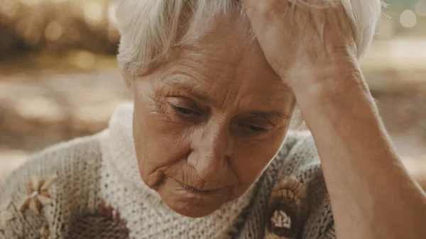 Портрет пожилой обеспокоенной женщины, держащей руку над лбом в парке — стоковое фото