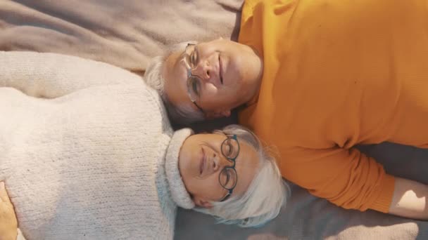 Nyugdíjas pár élvezi az őszi napokat a parkban. Feküdni a takarón és egymásra nézni. — Stock videók