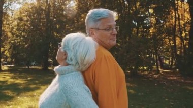 Yaşlılıkta aşk ve romantizm. Emekli çift ormanda sonbahar gününün tadını çıkarıyor sırt sırta verip gülümsüyor.