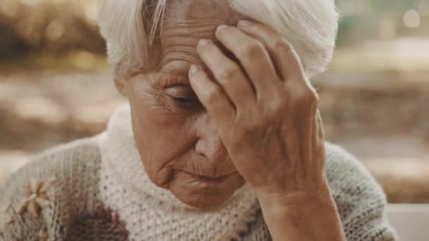 Vieja mujer de pelo gris preocupada sentada en el banco y rezando — Vídeos de Stock